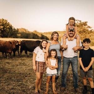 A family posed standing in a field in front of cows.