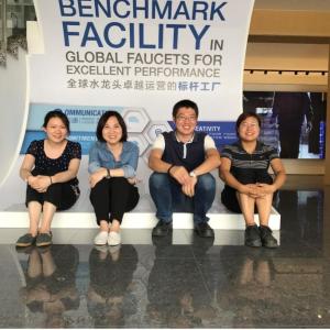 Four people seated in front of a sign "Benchmark facility in global faucets for excellent performance."