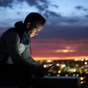 A person looking at a device in the dark. A city scape behind them.