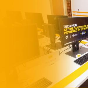 a staff member standing over a student working on a Tech Hub computer