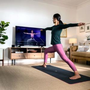 a person doing a yoga pose on a mat in a living room, watching an instructor on a tv screen