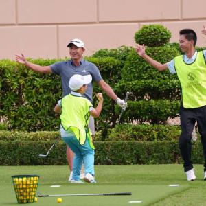 Adults and a child jumping in excitement, holding golf clubs on a green.