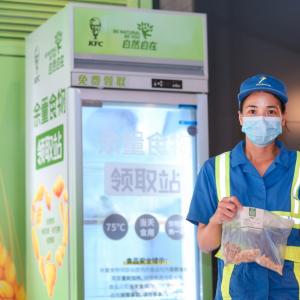 worker stands with a bag of food in front of a food bank refridgerator