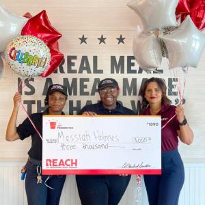 3 people hold a big check and balloons together 