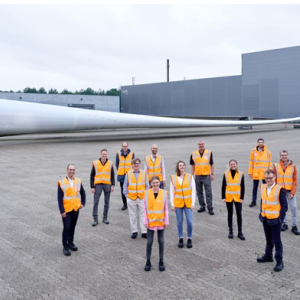 A group posed standing outside in front of a huge wind turbine blade.