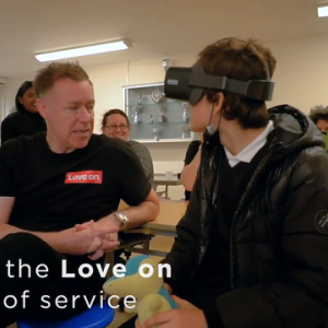 Person in VR headset facing a man in a Lenovo t-shirt