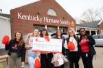 Six people standing together outside in front of the Kentucky Human Society, holding a large check