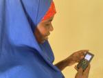 A woman holds a small cellphone in front of a yellow wall. 