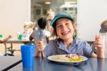 Smiling student sitting at table with a school lunch 
