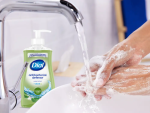 Someone washing their hands under running water, with a bottle of Dial Antibacterial Defense in the background