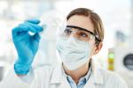 A scientist in protective gear looking at a petri dish