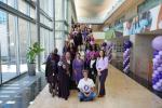 A group of people posed next to purple balloons and big windows