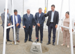 Six people smiling and gathered around a weight on a cable as one lowers it into the ground