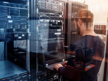 A person with a laptop working in a server room.