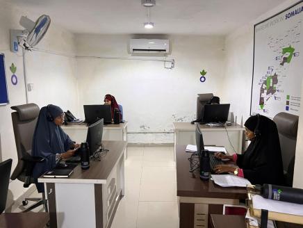 Three women work at desks in a white room in the call center. 