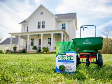 A bag of Scotts Grass Seed next to a spreader, in front of a house