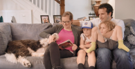 Cara and family seated on a couch reading a book.