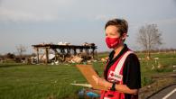 Red Cross volunteer carries a clip board in a field with debris scattered