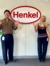 two interns waving in front of Henkel sign