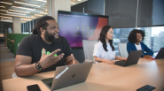 Three people at a long desk. A digital screen behind them.