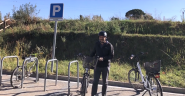 A smiling person standing by a bicycle in a bike parking area.