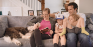 Cara and family seated on a couch reading a book.