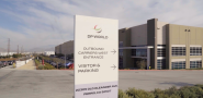 A DP World logistics facility in Perris, California, featuring a sign at the entrance directing outbound carriers and visitors to parking, with the warehouse and loading areas visible in the background under a clear sky.