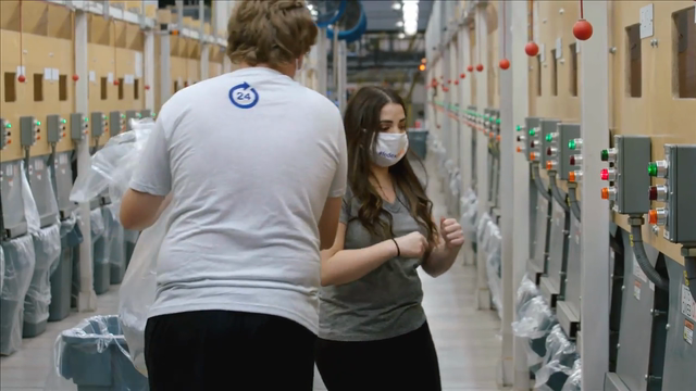Image of a woman wearing a face mask and a man walking towards her with his back turned to the camera