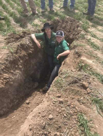 Kate Indreland, with agroecologist Nicole Masters (left), in a soil pit in Turner, Montana, examining wheat in a conventional operation to observe the hard pan tilling creates.