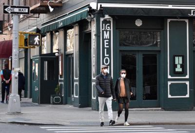 A couple in face masks walk past the J.G. Melon restaurant at the crossing of Third Avenue and East 74th Street on the Upper East Side of Manhattan during the pandemic of the novel coronavirus disease (COVID-19). The board in the centre shows a message reading "Please, avoid close contact with people who are sick". As of 13 April 2020, the United States has reported more than 560,000 confirmed cases of the novel coronavirus infection, with more than 104,000 confirmed cases in New York City. (Photo by Maria Khrenova\TASS via Getty Images)