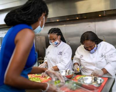 Culinary Director Quin Kelly (left) provides tips on chopping vegetables while prepping meals with students.