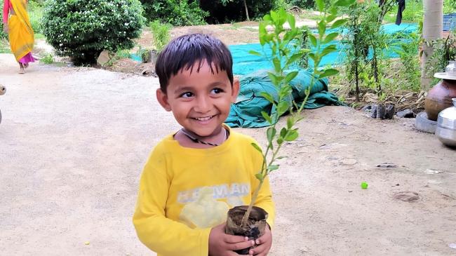 Child smiling holding a tree sapling