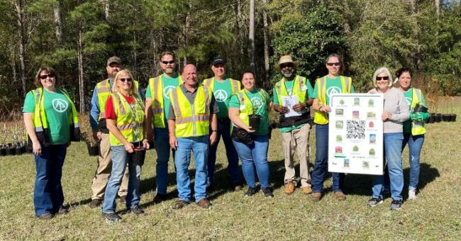 International Paper volunteers in safety vests holding potted trees and a poster of the kinds of trees planted