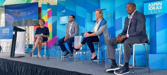 Four people on stage seated. Aspen Ideas Health on many screens behind them