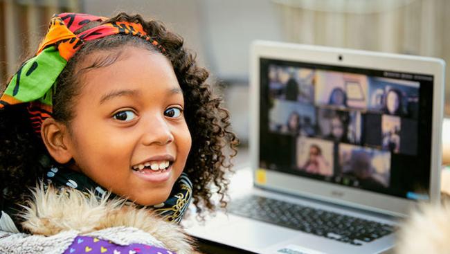 Young black student seated in front of a laptop smiling.