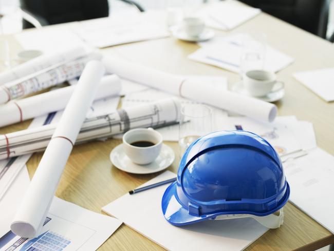 Desk littered with rolls of paper, a coffee cup, and a hard hat