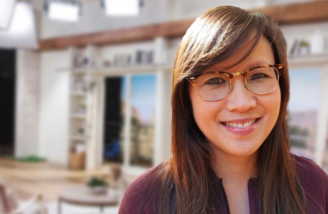 A photo of Virginia Nguyen with brown hair, wearing glasses and a maroon top while on-set at QVC Studios