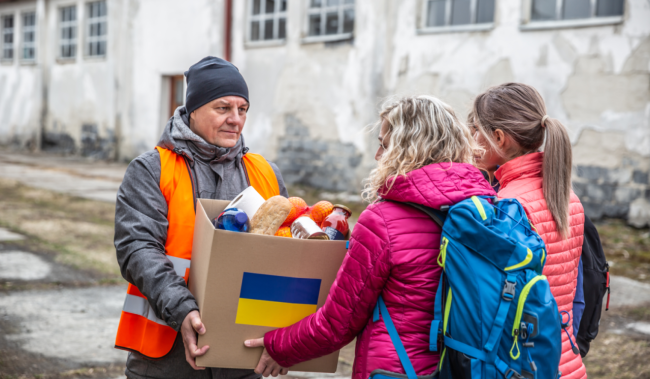 two women giving a box of donations to a man 