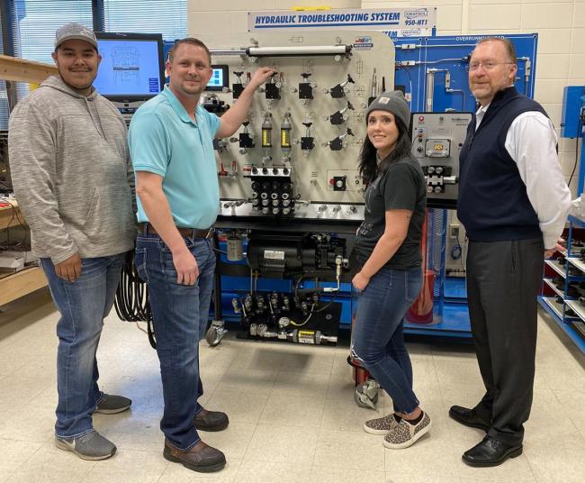 Four people in front of manufacturing equipment