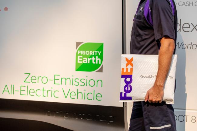 FedEx worker carrying a package in front of a zero-emission all-electric vehicle