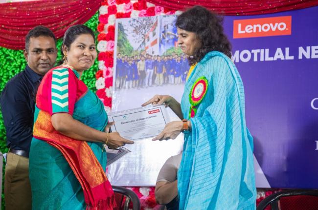 a person accepting a certificate from another, a large colorful banner behind them