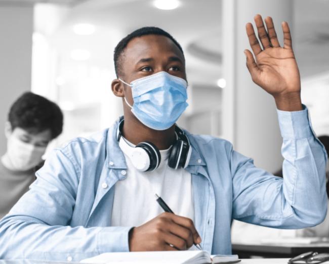 Black student in a blue shirt and mask raising their hand