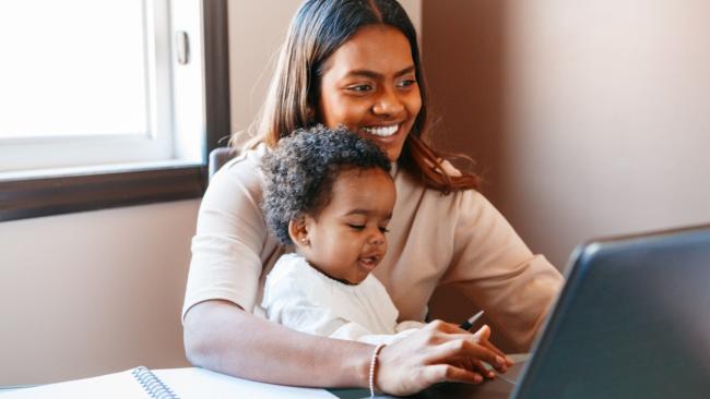 Smiling woman holding a young child while working on a laptop