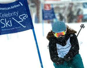 Guests race down the mountain to support Cystic Fibrosis Foundation. Person skiing next to a "celebrity ski" banner