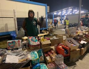 aide worker standing behind a row of boxes of supplies like diapers, water, soaps.