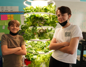 Two students pose with arms crossed in front of hydroponic classroom plants