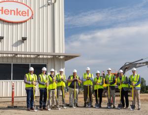 Group of ten people in hi-visibility vests holding shovels in front of new Henkel facility