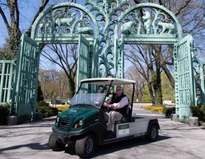 Jim Breheny, director of the Bronx Zoo, sits in one of the new electric vehicles in front of two large gates.