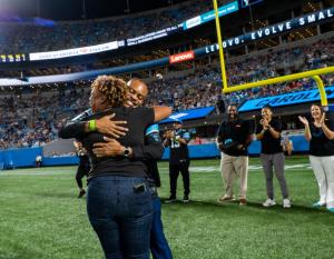Hip Hop Smoothies of Charlotte representative hugs Lenovo North America CMO Gerald Youngblood on the Carolina Panthers field