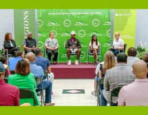A panel of Black leaders, athletes, and students on a raised platform in front of a green backdrop